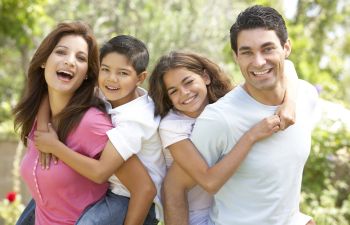 Happy parents piggybacking their little son and a daughter while having fun in a park., 