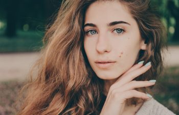 Portrait of a beautiful authentic curly-haired girl in the park in a light beige sweater with blue eyes and birthmarks on her face. No makeup.